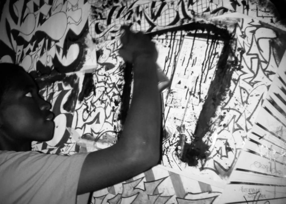 Šhema painting a mural with graffiti designs on a wall